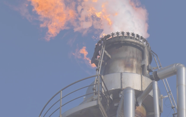 A large industrial smokestack emits flames and smoke, excelling against a clear blue sky.