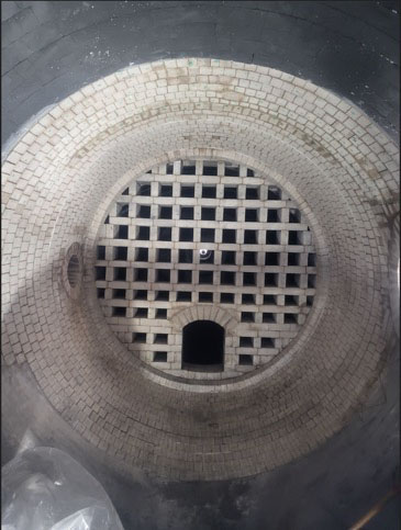 View of a circular brick kiln or furnace interior with a grid pattern floor and a small arched opening at the bottom center.