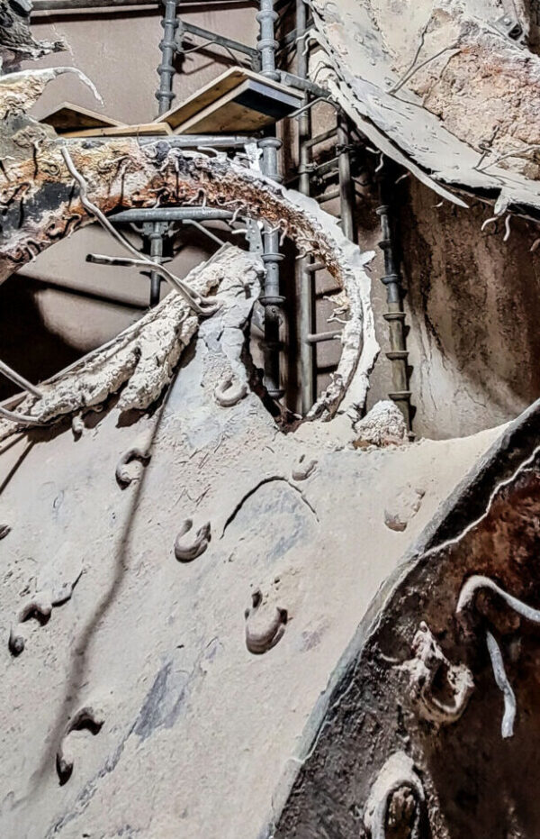 Close-up of exposed rebar and damaged concrete with cracks, rough textures, and some crumbling debris visible.